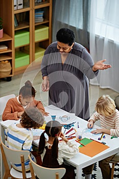 Black mature woman as female teacher helping little children at preschool