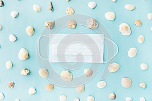 Black medical face mask and seashells on blue background. Flat lying, copy space, holiday cancellation, pandemic, tourism