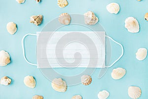 Black medical face mask and seashells on blue background. Flat lying, copy space, holiday cancellation, pandemic, tourism