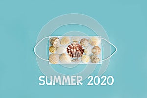 Black medical face mask and seashells on blue background. Flat lying, copy space, holiday cancellation, pandemic, tourism