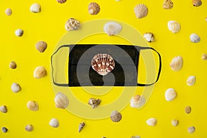 Black medical face mask and seashells on a yellow background. Flat lying, copy space, holiday cancellation, pandemic, tourism