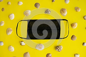 Black medical face mask and seashells on a yellow background. Flat lying, copy space, holiday cancellation, pandemic, tourism