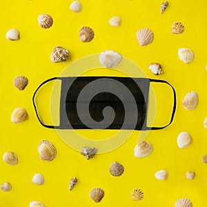 Black medical face mask and seashells on a yellow background. Flat lying, copy space, holiday cancellation, pandemic, tourism