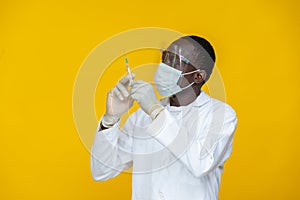 Black medical personnel, wearing a lab coat, and protective gear, holding and looking closely at a syringe