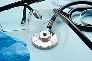 Black medical stethoscope, plastic safety goggles on blue background