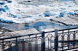 Black metal fence of the city embankment. Spring river Amur during ice drift.