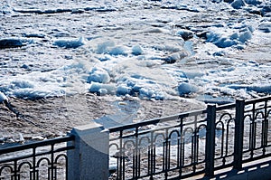 Black metal fence of the city embankment. Spring river Amur during ice drift.