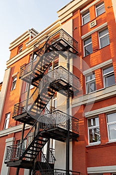 Black metal fire escape on the facade of a red old building. Renovation.