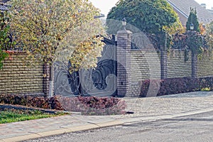 Black metal gate and brown brick fence in the autumn street