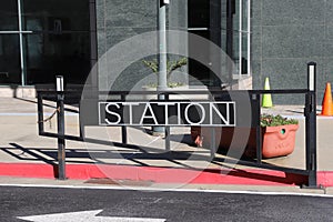 A black metal gate with the word `Station` on the front surrounded by street cones a red curb and black building photo