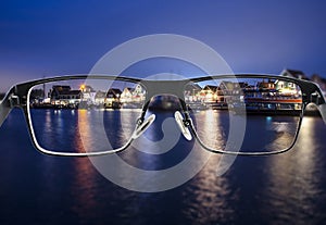 Black metal glasses looking through colorful night cityscape