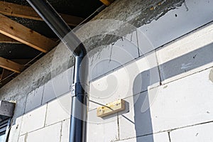 A black metal gutter attached to the raw wall of the house to make a distance to insulate the building.