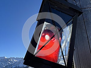 A black metal lantern with a red candle on a wooden crucifix with a wonderful winter panorama of the snow-covered Arosa