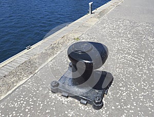 Black metal mooring bollard in marina and port terminal. Close up of mooring noray on a dock. Port conditioning photo