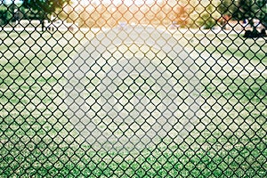 Black metal netting wire mesh fence against green field meadow. Texture pattern surface background