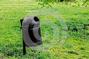 Black metal tresh bin on green grass.