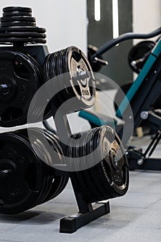 Black metal weight plates for barbell are located on rack in sports complex.