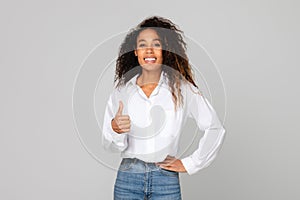 Black millennial lady showing thumbs up gesture over gray background