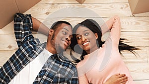 Black millennial woman with her boyfriend lying among carton boxes on floor of their new house, top view