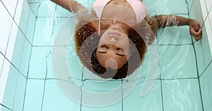 Black mixed race woman swin towards a camera on back with closed eyes