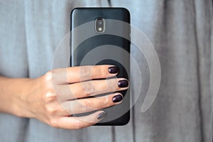 Black mobie smart phone in woman/s hands with perfect dark violet manicure