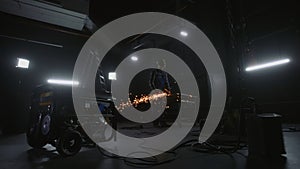 Black mobile gasoline power generator in a dark workshop. In the background, a man in blue overalls, a hard hat and