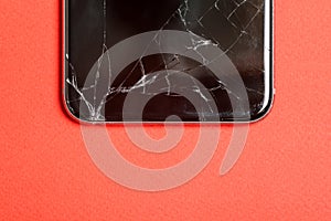 Black mobile phone or tablet with a broken screen. Smartphone on a red background close-up. Broken screen glass
