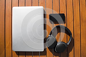 Black mobile phone, tablet, metallic laptop outdoor on an orange wooden table