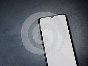 Black mobile smartphone mockup lies on the surface with a blank screen isolated on a dark marble stone background