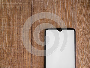Black mobile smartphone mockup lies on the surface with blank screen isolated on wooden background