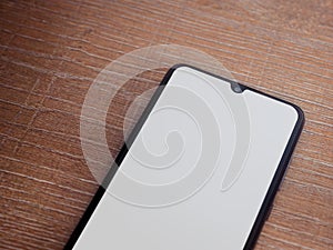 Black mobile smartphone mockup lies on the surface with blank screen isolated on wooden background