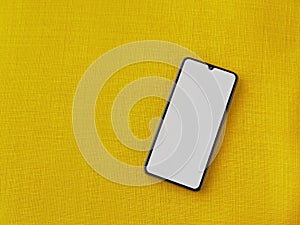 Black mobile smartphone mockup lies on the surface with a blank screen isolated on a yellow fabric background