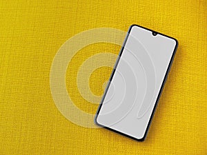 Black mobile smartphone mockup lies on the surface with a blank screen isolated on a yellow fabric background