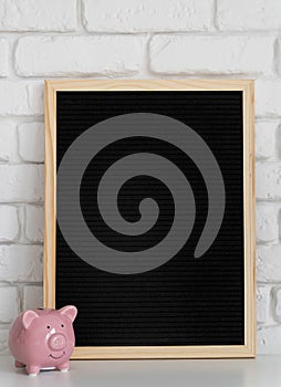 Black mock up felt letter board with small piggy bank on white brick background