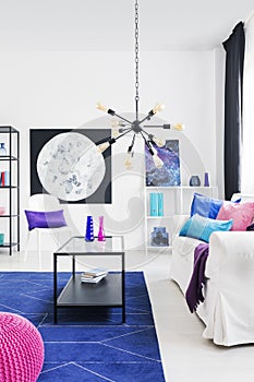 Black modern chandelier with yellow bulbs in cosmos inspired living room with moon graphic, metal coffee table and white sofa with