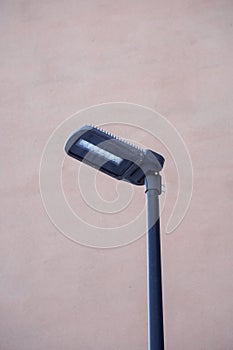 Black modern LED street lamp, lantern towards pink facade wall during the day time.