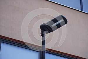 Black modern LED street lamp, lantern towards pink facade wall during the day time and white window.