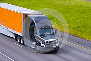Black modern semi truck orange trailer driving highway line