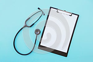 Black modern stethoscope and blank medical form on light blue background