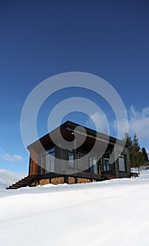 Black modern tiny cabin in snowy weather with blue clear sky