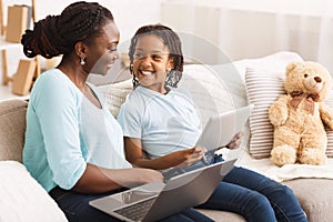 Black mom and daughter browsing Internet on sofa