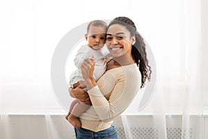 Black Mom Holding Little Infant Smiling To Camera Posing Indoors