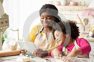 Black mom and little daughter checking dough recipe online on digital tablet