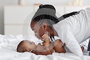 Black mom playing in bed with her infant, kissing baby