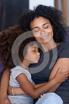 Black mom and small daughter hugging tenderly on couch