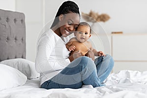 Black mommy sitting with her cute little infant on bed