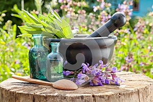 Black mortar with sage herbs, glass bottles of essential oil