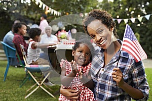 Black mother and baby hold flag at 4th July party, to camera