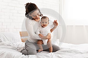Black Mother Playing With Infant Baby Son Sitting In Bed