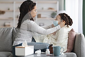 Black mother putting face mask on her sick little daughter